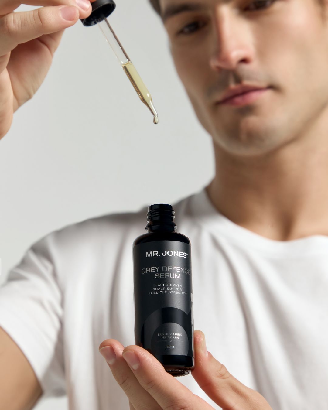 Person holding a bottle of 'MR. JONES GREY DEFENCE SERUM' with a dropper.