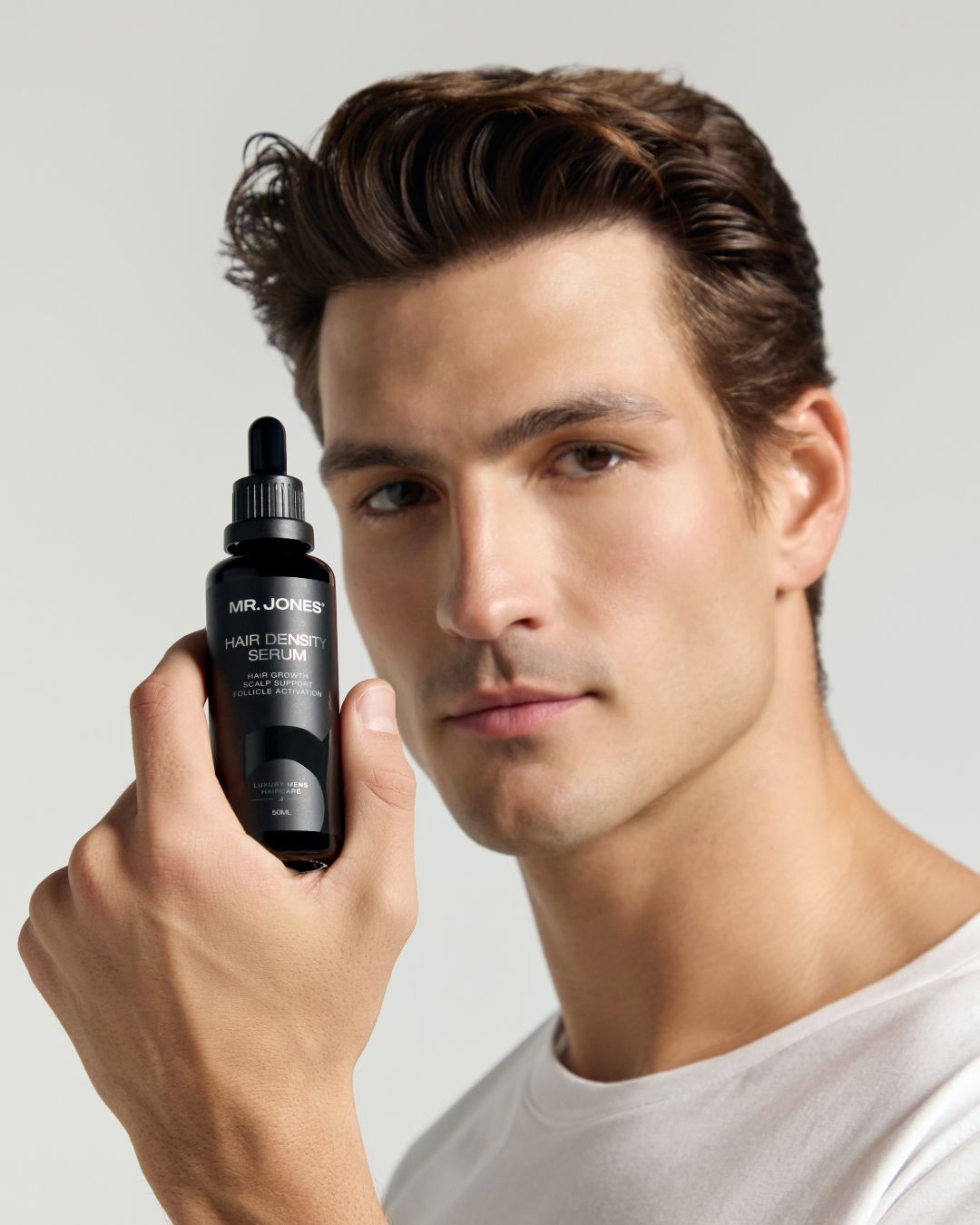 Man holding a bottle of Mr. Jones hair density serum against a neutral background