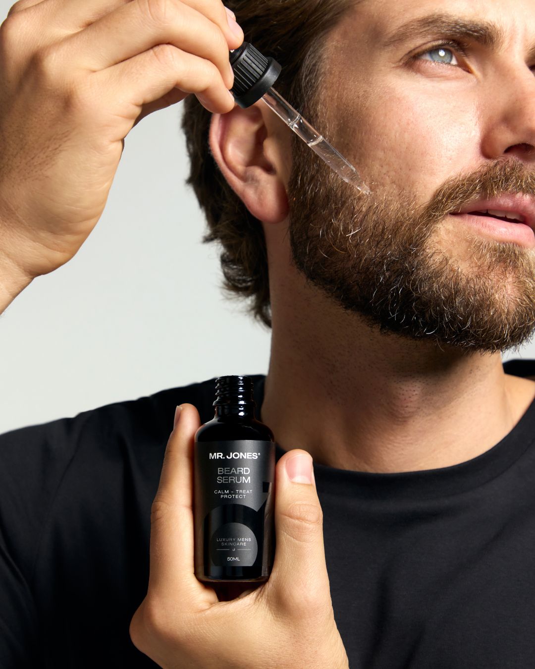 Man applying beard serum from a dropper bottle to his beard.